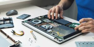 A person works on an open laptop’s internal components, replacing or repairing parts with tools laid out nearby