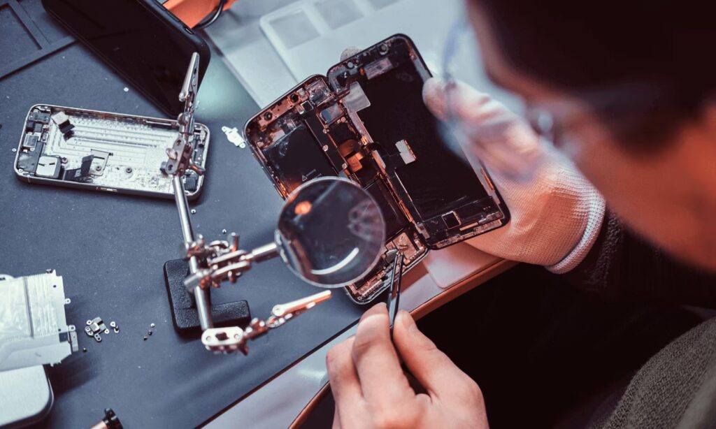 Close-up of iPhone repair process using a magnifying glass to inspect internal components.