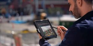Man using a stylus to work on a rugged tablet outdoors, viewing a detailed technical diagram on the screen
