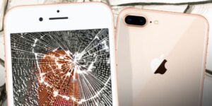 Close-up of a cracked iPhone screen next to an undamaged iPhone showing front and back views of the same model on a light background