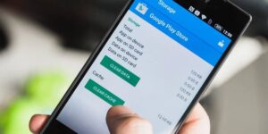 A person holding a smartphone showing the storage settings for Google Play Store with options to clear data and clear cache selected