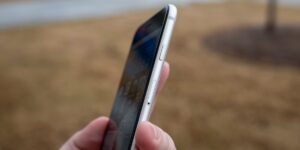 Close-up of a hand holding a smartphone outdoors, focusing on the side with volume and power buttons and a visible SIM card tray