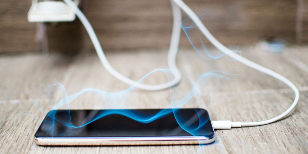 Smartphone connected to a charger, lying on a wooden floor with blue smoke or electric current effects rising from it