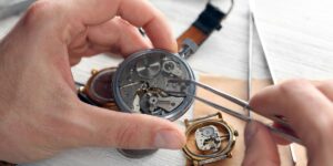 Hands of a watchmaker using tweezers to repair the intricate mechanical gears of a small watch movement