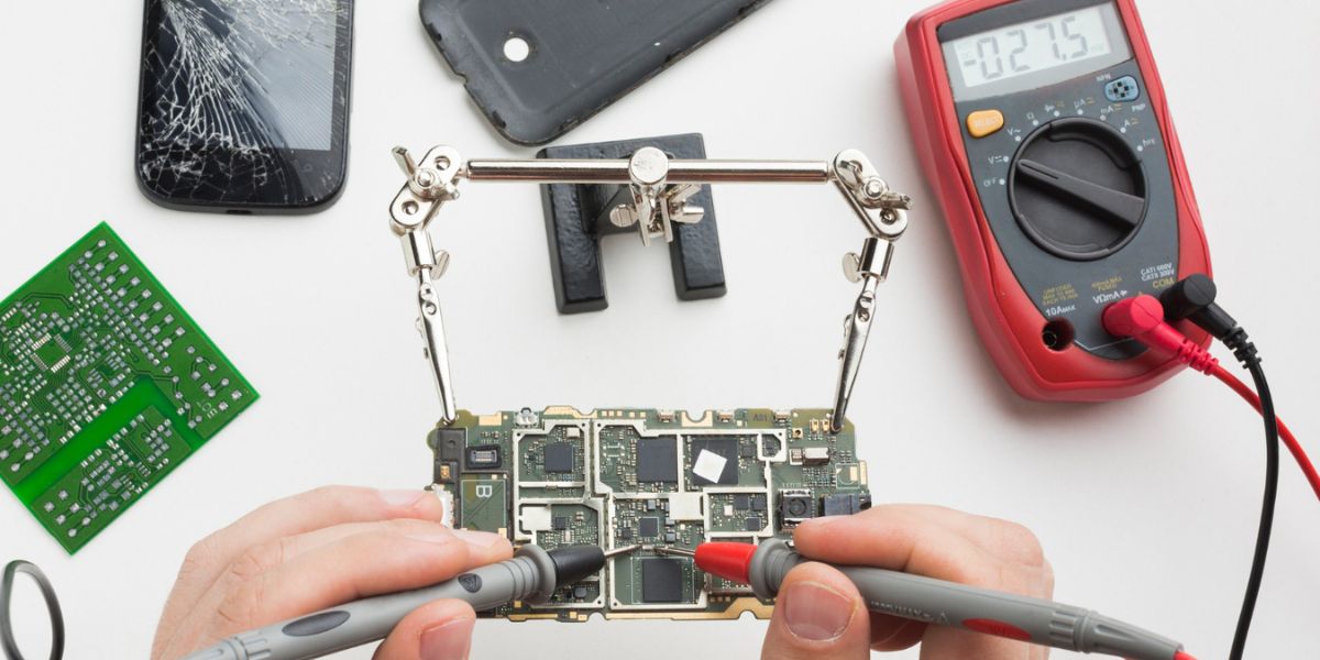 Technician's hands using probes and a multimeter to test a mobile device circuit board
