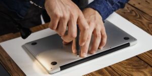 A technician uses a precision screwdriver to remove the bottom panel of a silver laptop on a white workspace