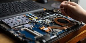 A technician uses a precision screwdriver to repair the internal motherboard and cooling fan of an open laptop