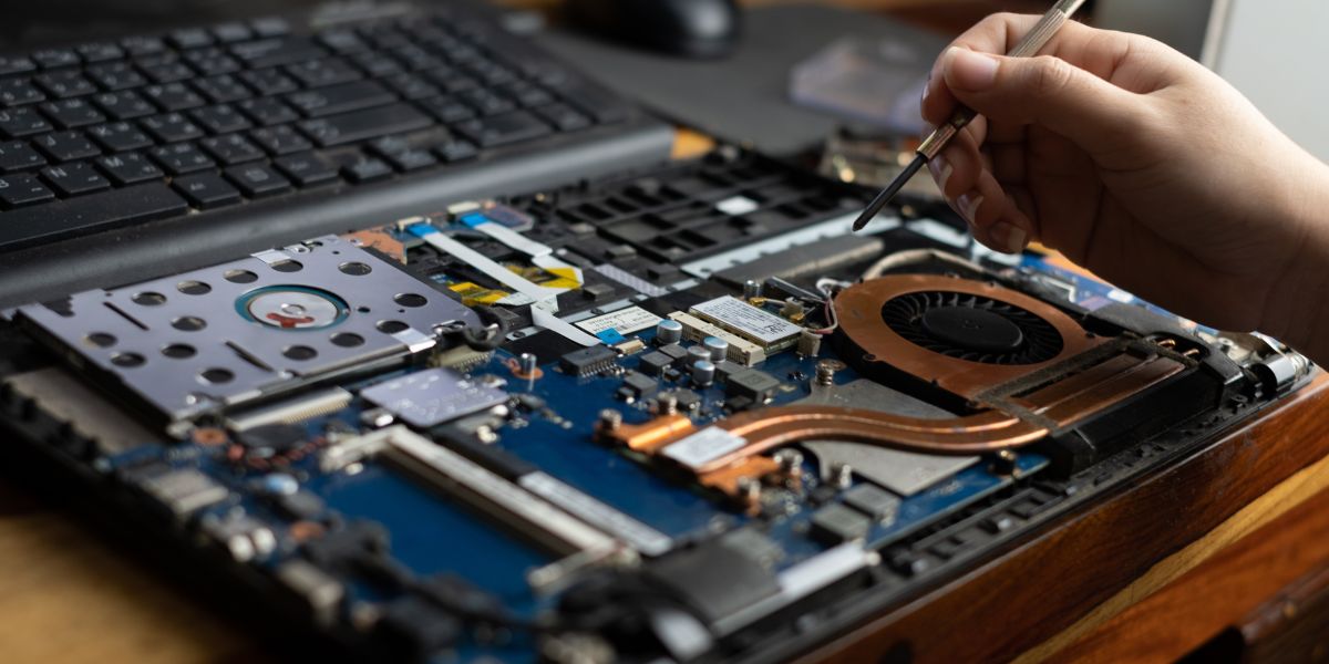 A technician uses a precision screwdriver to repair the internal motherboard and cooling fan of an open laptop