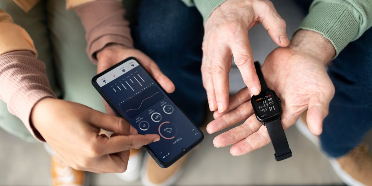 Two people compare fitness data on a black smartphone and a black smartwatch, showing synced health progress stats