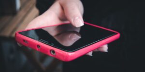 A person's hands holding a smartphone with a pink case, their thumb touching the dark, reflective screen surface