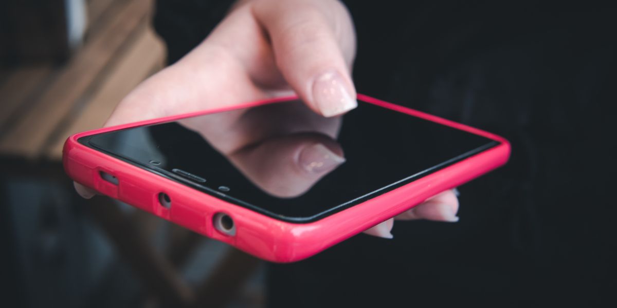 A person's hands holding a smartphone with a pink case, their thumb touching the dark, reflective screen surface